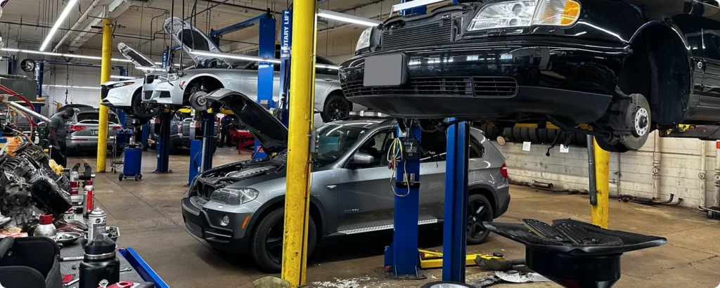 Diagnostics and electrical repair in Milwaukee, WI. Cars lifted on platforms in a busy auto repair shop, mechanics working under them with tools and car parts visible.