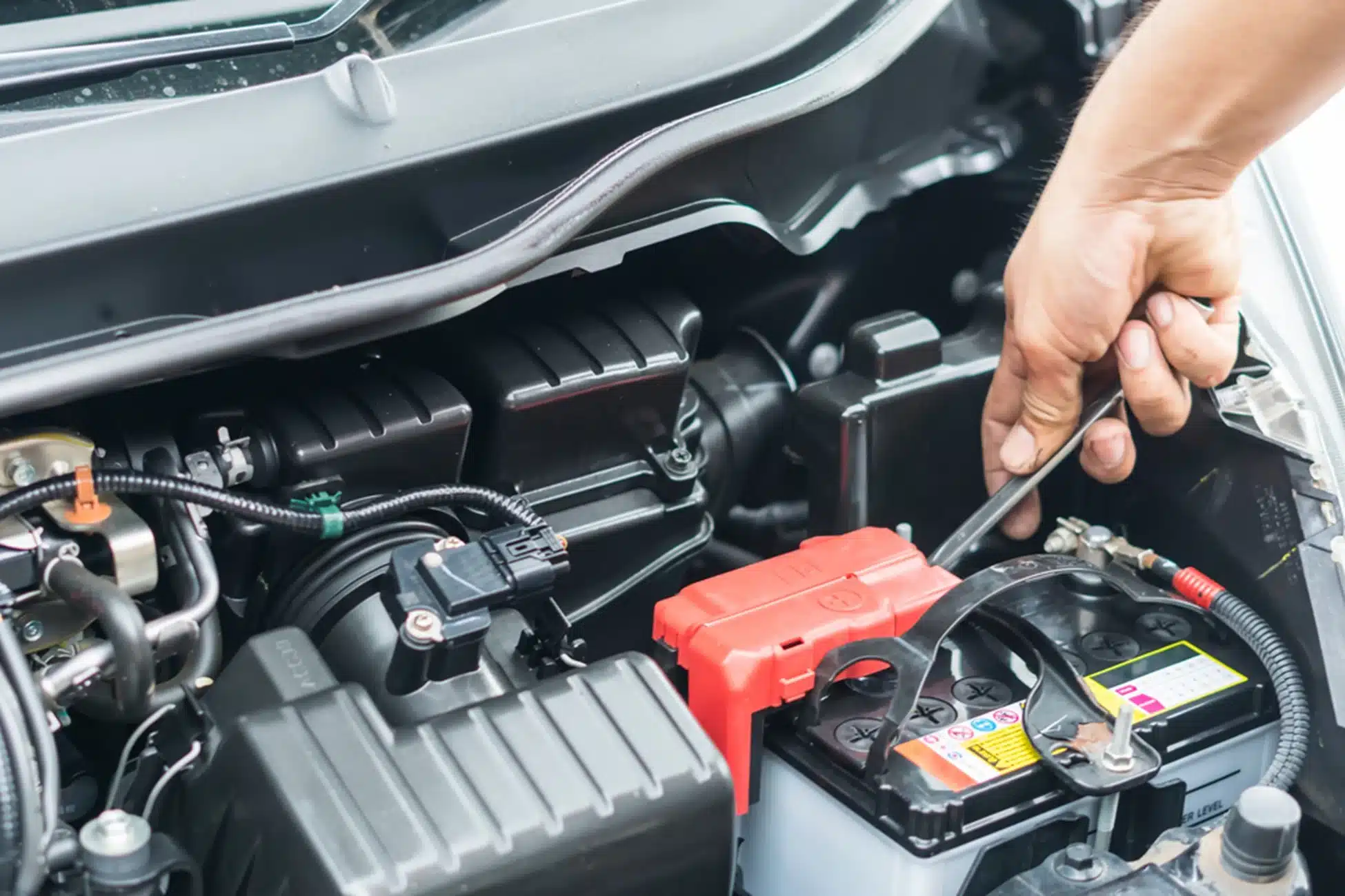 Electrical Maintenance by O'Reilly Motor Cars in Milwaukee, WI: Close-up of a hand tightening a battery terminal connection in a car engine bay, highlighting the importance of maintaining electrical systems during summer heat to prevent breakdowns and ensure optimal performance.