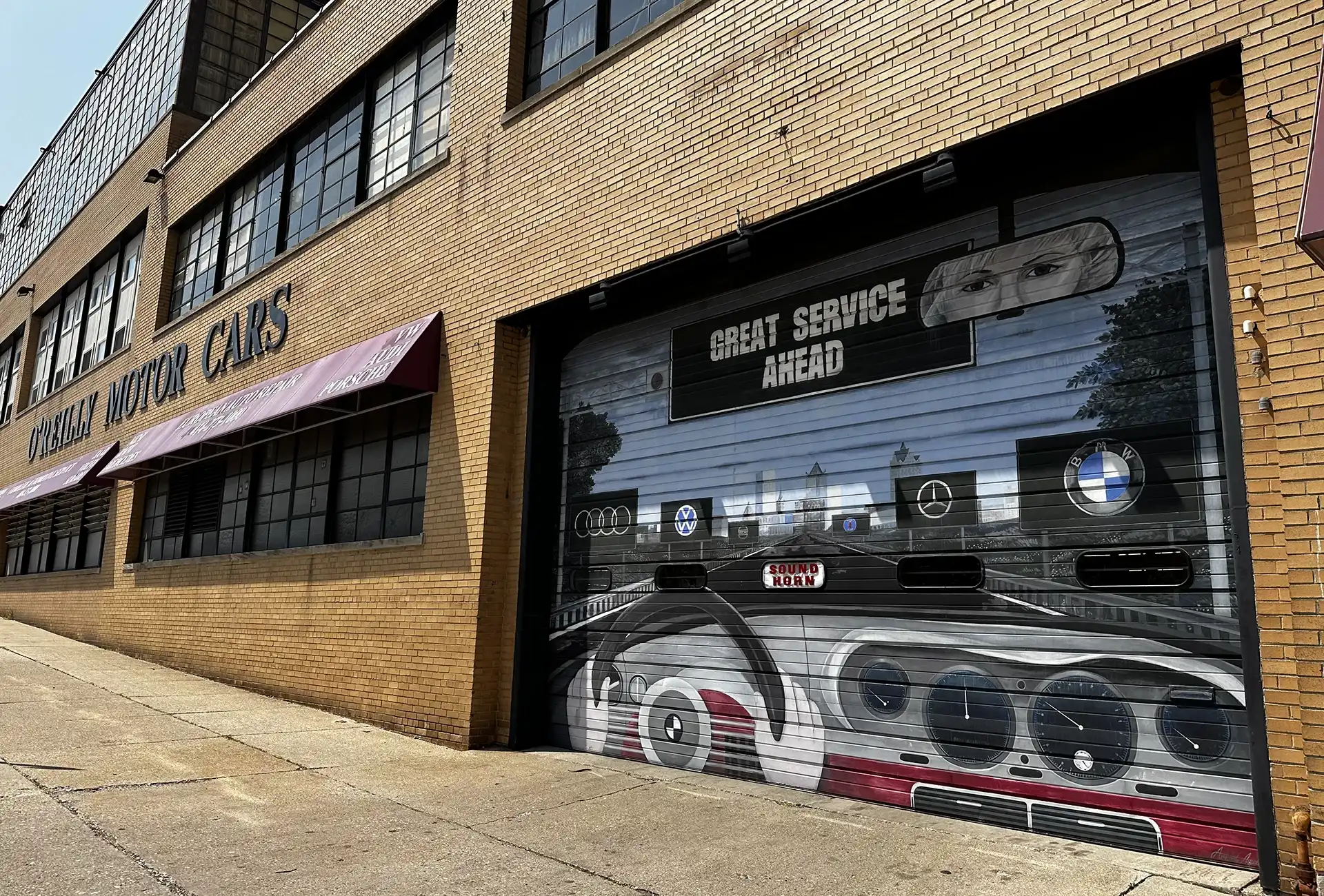 Garage with a mural featuring car logos and "Great Service Ahead" text on the door at a building labeled "Gulak Motor Cars.