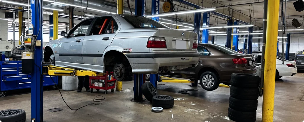 Cars lifted on hydraulic lifts in an auto repair shop, with tools and spare tires scattered around the garage.