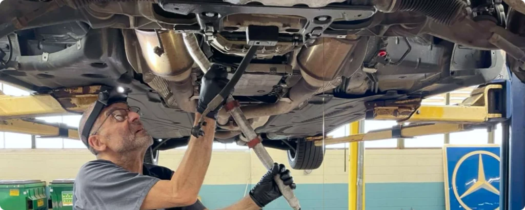 Fluid exchange services for vehicles in Milwaukee, WI. with O'Reilly Motor Cars. Mechanic working underneath a car on a lift, holding a tool and wearing a headlamp for better visibility.