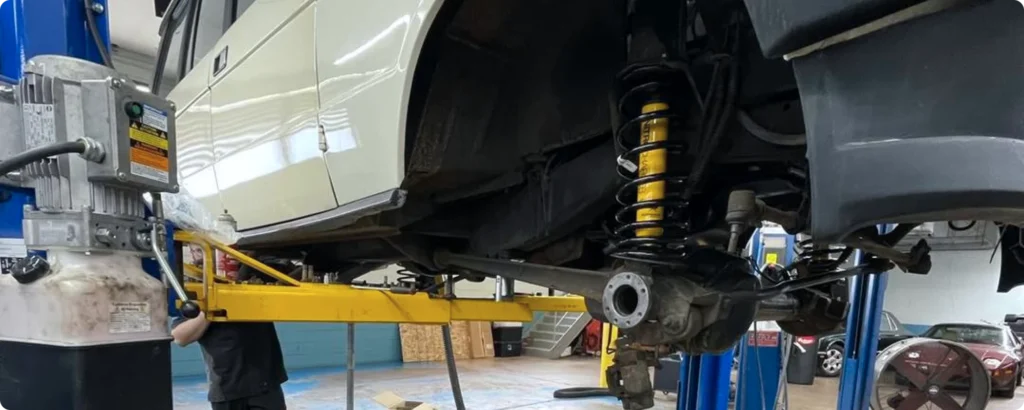 Steering and suspension check in Milwaukee, WI. Mechanic working underneath a raised vehicle on a lift in an auto repair shop. Visible suspension and lift equipment.