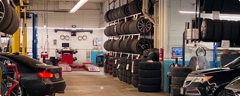 Wheel alignment in Milwaukee, WI. A busy auto shop with stacks of tires on shelves, a black car, and a tire alignment machine in the background.