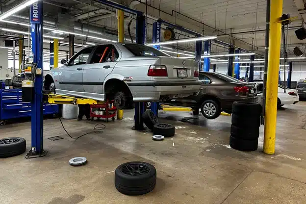 Which brand is better BMW or Mercedes-Benz in Milwaukee, WI with O’Reilly Motor Cars. Image of silver BMW raised in the air on car lift with tires off in shop for brake services with a gray and white vehicle on other lifts in the shop bay in the background.