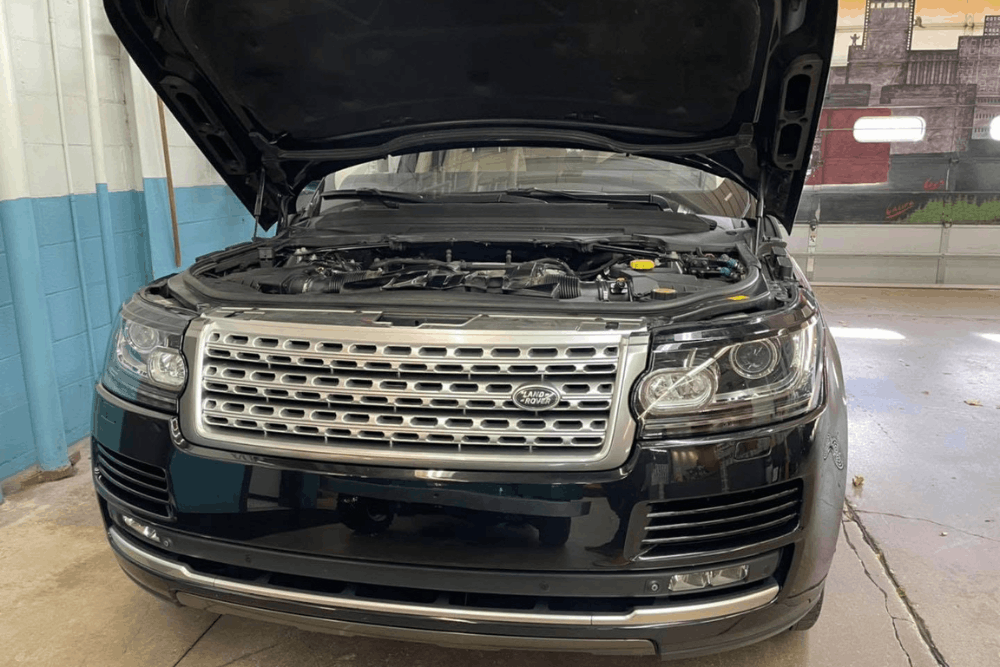 Land Rover repair in Milwaukee, WI at O'Reilly Motor Cars. Image of a black Land Rover with the hood open inside the shop, showing the engine bay during inspection and service.