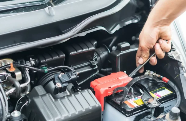 Electrical Maintenance by O'Reilly Motor Cars in Milwaukee, WI: Close-up of a hand tightening a battery terminal connection in a car engine bay, highlighting the importance of maintaining electrical systems during summer heat to prevent breakdowns and ensure optimal performance.