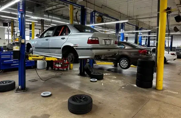 Which brand is better BMW or Mercedes-Benz in Milwaukee, WI with O’Reilly Motor Cars. Image of silver BMW raised in the air on car lift with tires off in shop for brake services with a gray and white vehicle on other lifts in the shop bay in the background.